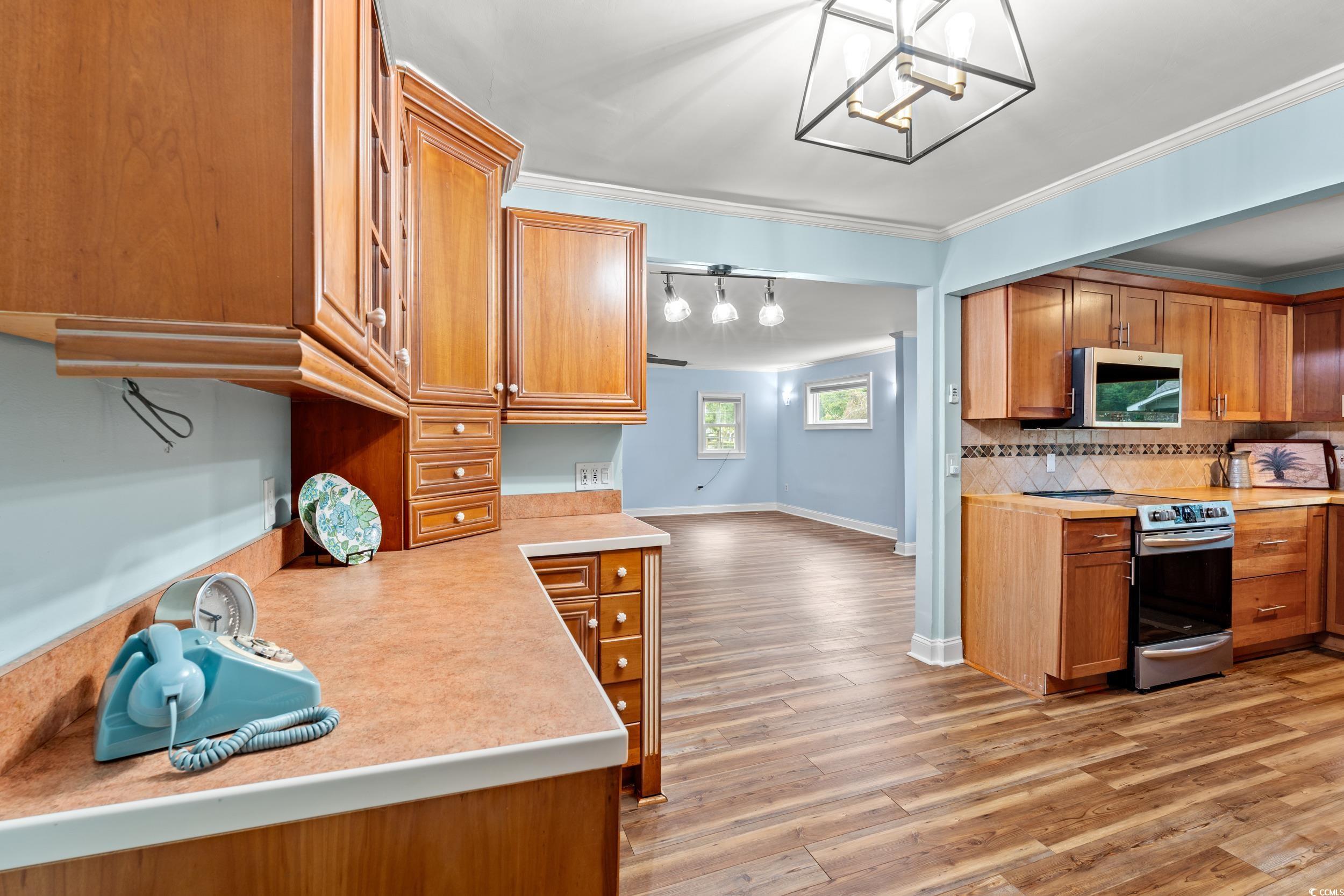 902 Palm Street Georgetown, SC 29440 - Photo 10 of 38 Kitchen with light countertops, light wood finished floors, appliances with stainless steel finishes, brown cabinetry, and crown molding