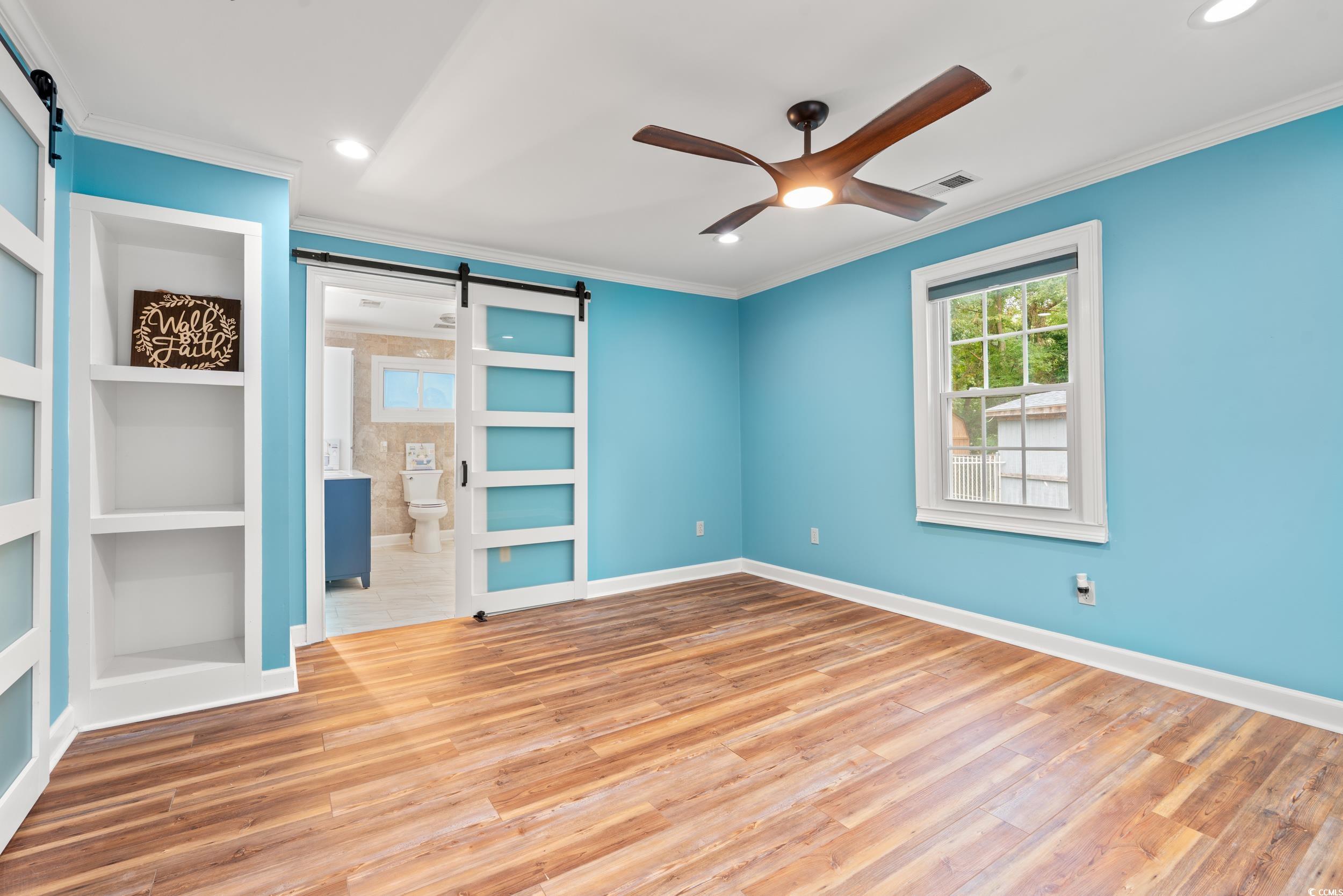 902 Palm Street Georgetown, SC 29440 - Photo 15 of 38 Unfurnished room with a barn door, built in shelves, ornamental molding, light wood-style flooring, and a ceiling fan