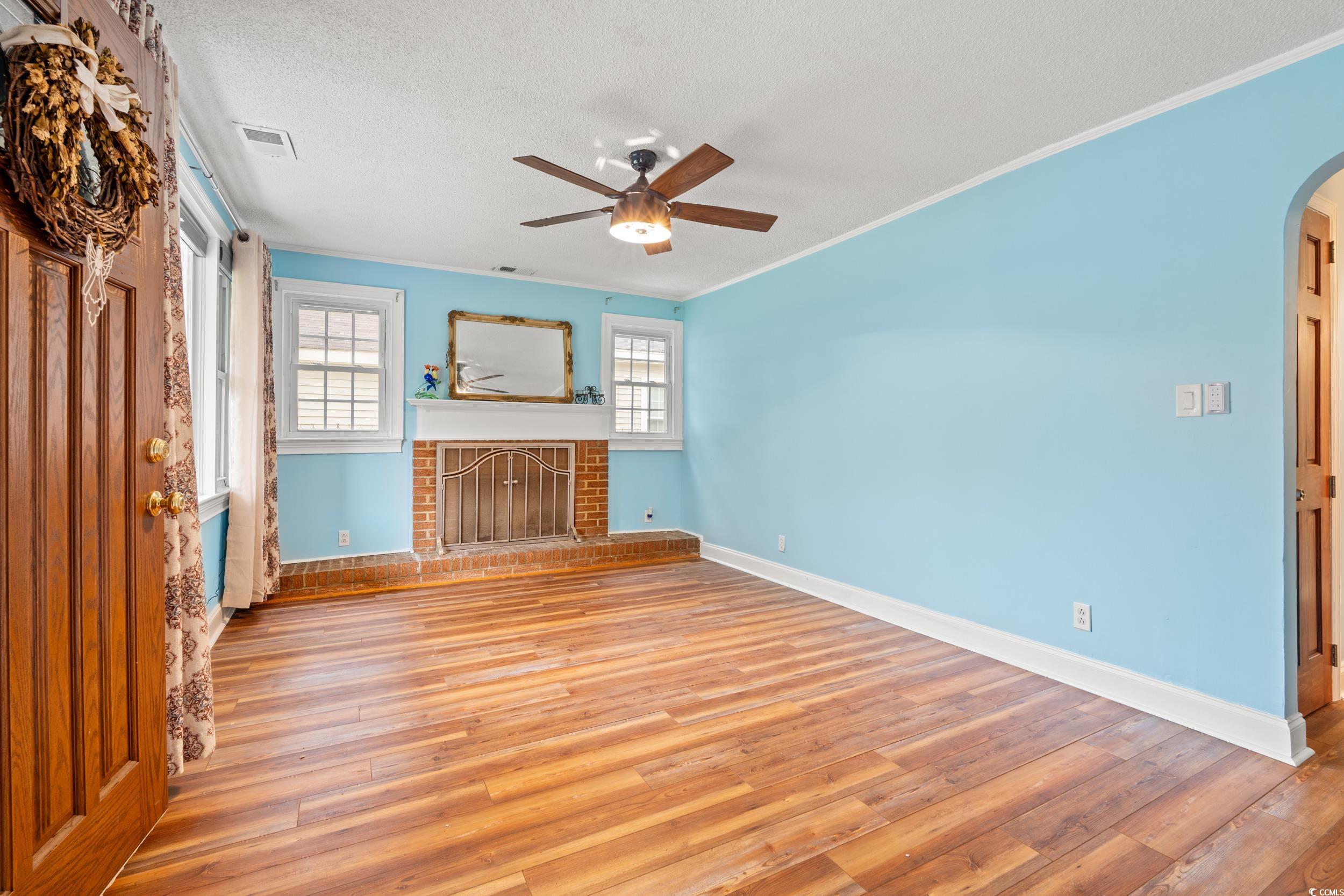 902 Palm Street Georgetown, SC 29440 - Photo 5 of 38 Unfurnished living room with light wood finished floors, arched walkways, a fireplace, ornamental molding, and a textured ceiling