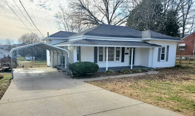 a view of a white house with a large tree and wooden fence