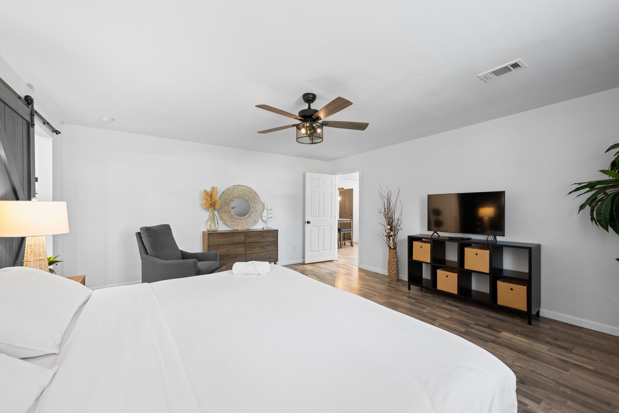 729 Kyle Angleton, TX 77515 - Photo 21 of 36 This spacious bedroom features modern decor with a ceiling fan, ample natural light, and a neutral color palette. It includes a cozy seating area, TV stand, and stylish storage, creating a comfortable and inviting atmosphere.