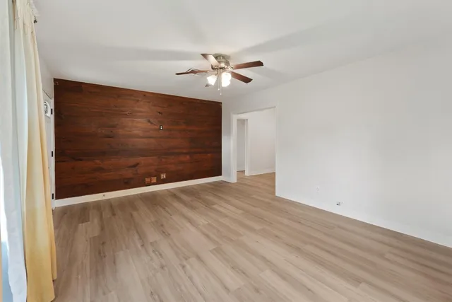 a view of an empty room with wooden floor and a ceiling fan