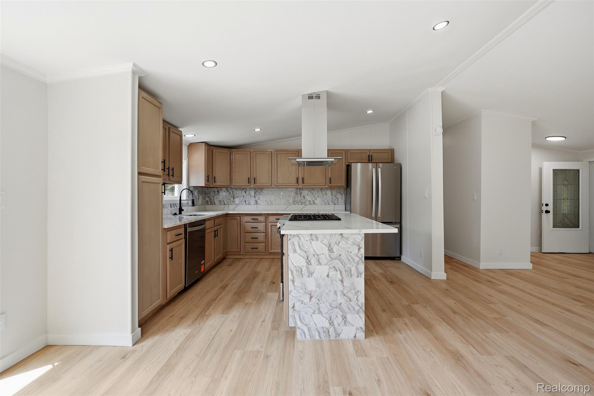 4420 Dublin Road Burton, MI 48529 - Photo 14 of 56 Open-concept kitchen featuring an eat-at island with a waterfall edge, stainless steel appliances, light wood-finish cabinetry, a gas range with a range hood, and light wood-finish flooring