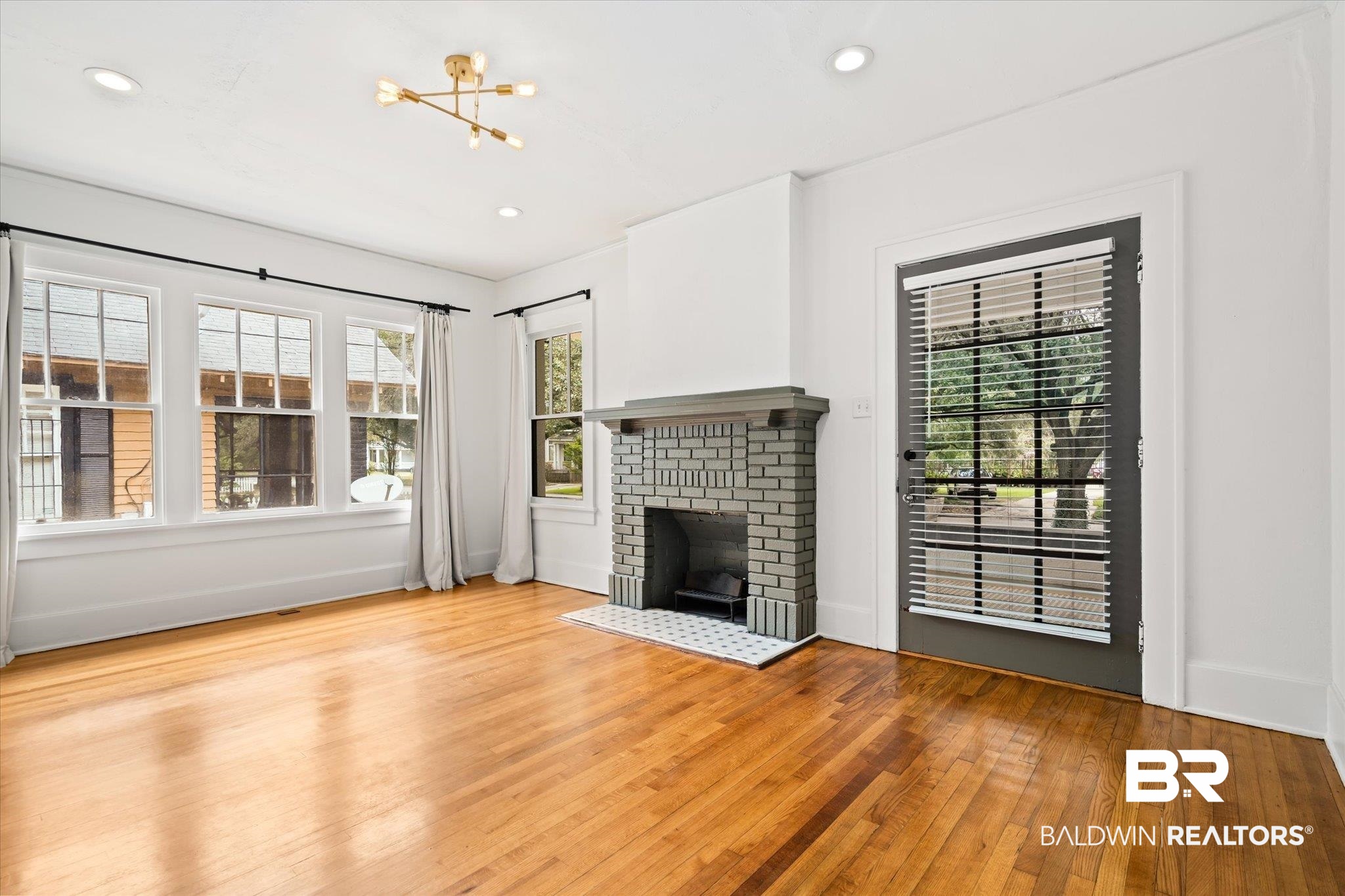 308 South Ann Street Mobile, AL 36604 - Photo 5 of 30 Unfurnished living room with a brick fireplace, a chandelier, and light hardwood / wood-style floors