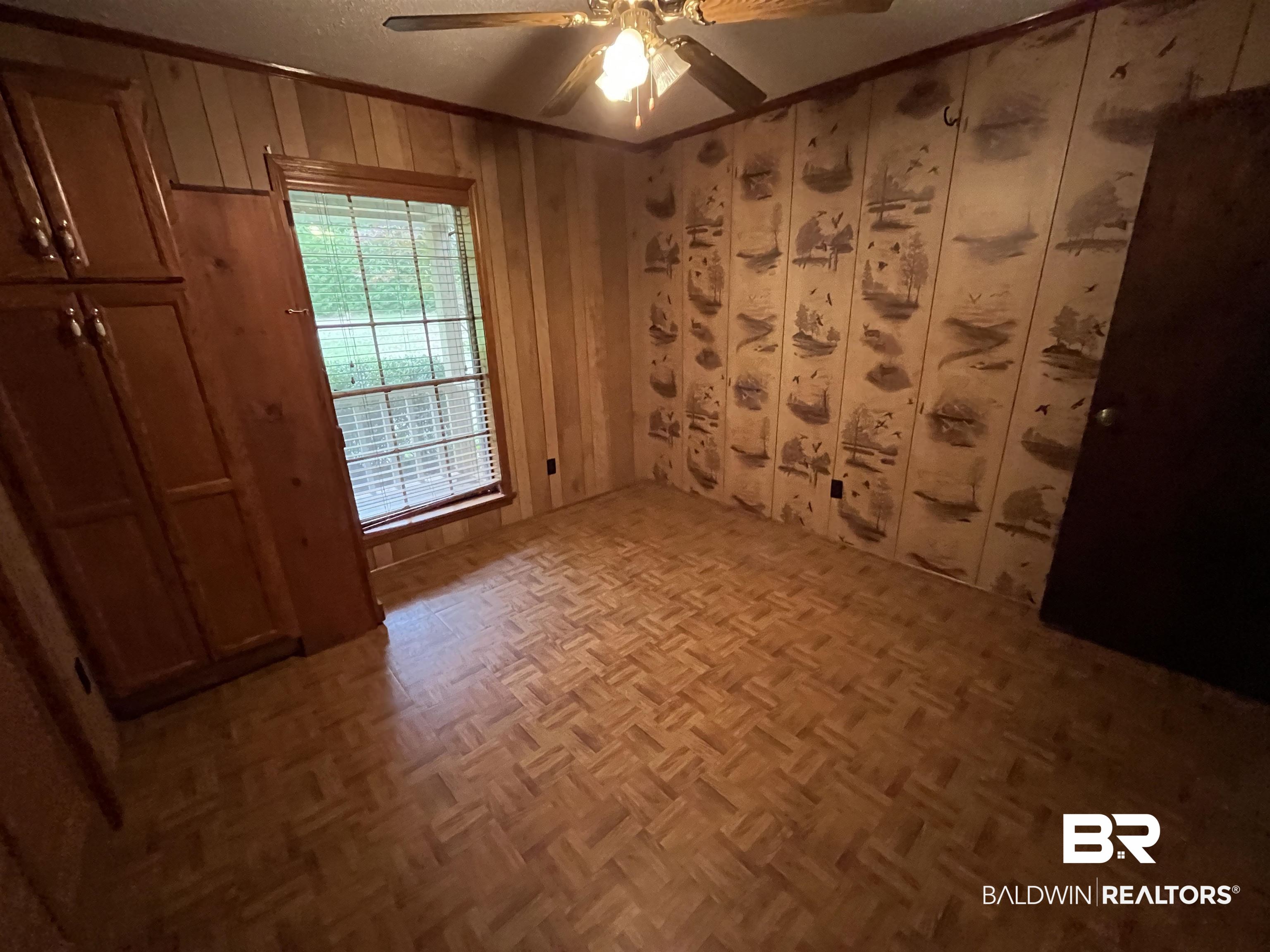 1905 Rockaway Creek Road Atmore, AL 36502 - Photo 19 of 23 Room featuring wood-finish parquet flooring, a wood-paneled wall, and a window with horizontal blinds