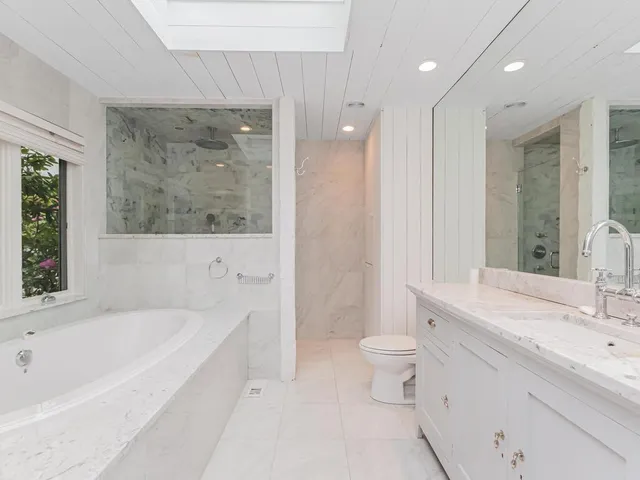 a bathroom with a bathtub shower sink vanity mirror and toilet