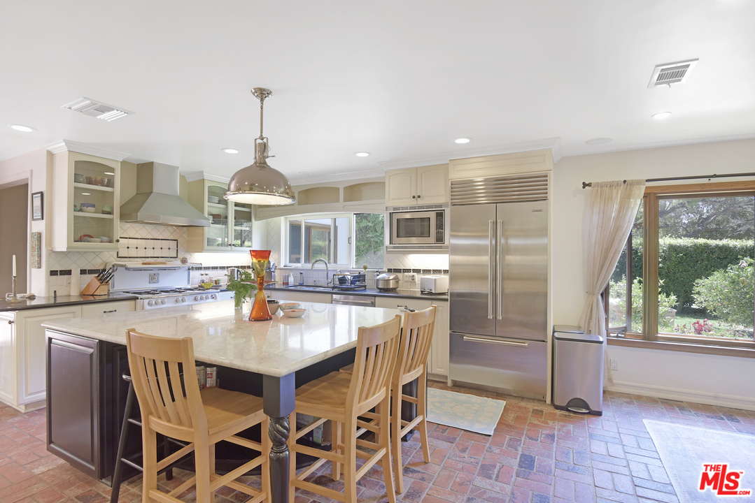 6138 Ramirez Canyon Road Malibu, CA 90265 - Photo 13 of 42 a kitchen with stainless steel appliances granite countertop a stove a refrigerator a sink a dining table and chairs with wooden floor