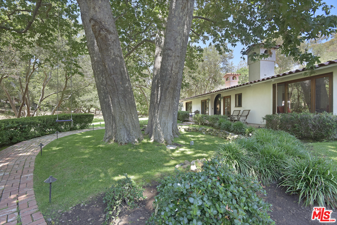 6138 Ramirez Canyon Road Malibu, CA 90265 - Photo 3 of 42 a backyard of a house with large trees and table and chairs