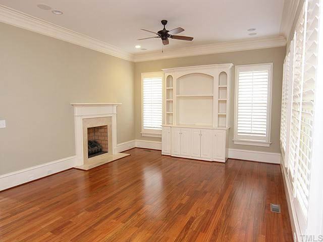 3112 Raymond Street Raleigh, NC 27607 - Photo 3 of 12 an empty room with wooden floor a fireplace and windows