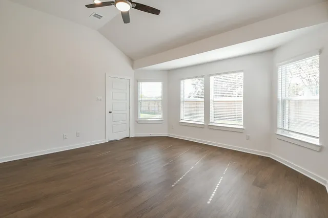 an empty room with wooden floor chandelier fan and windows