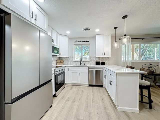 a kitchen with stainless steel appliances a refrigerator a stove a dining table and chairs with wooden floor