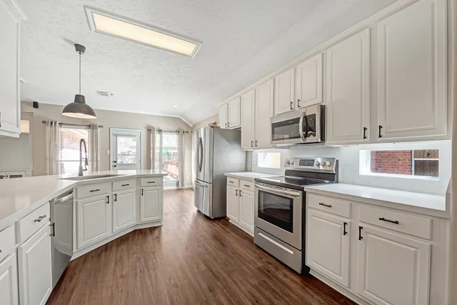 a kitchen with stainless steel appliances granite countertop white cabinets a sink a stove a refrigerator and white cabinets with wooden floor