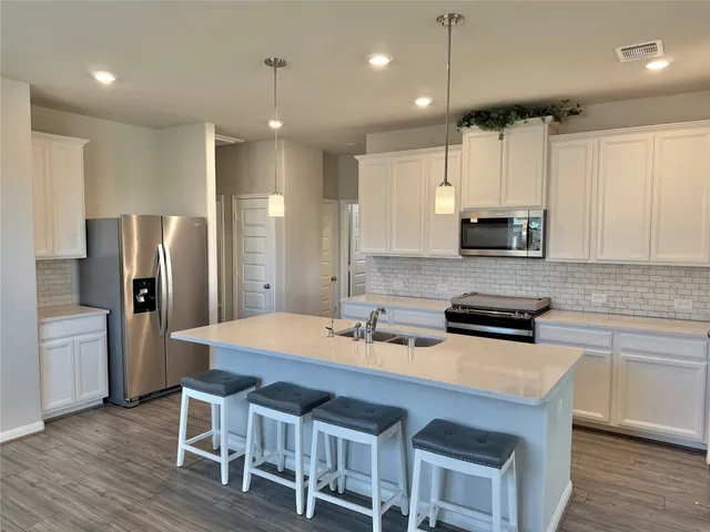 a kitchen with stainless steel appliances a stove a sink a microwave a refrigerator and white cabinets with wooden floor