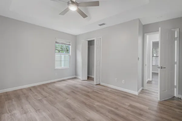 an empty room with wooden floor ceiling fan and windows