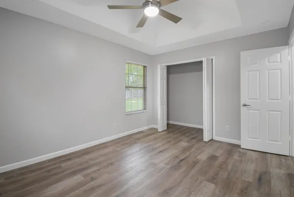 an empty room with wooden floor ceiling fan and windows