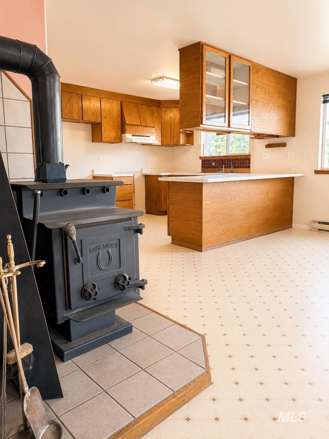 16434 Pride Lane Caldwell, ID 83607 - Photo 7 of 16 Kitchen area featuring a wood-burning stove with a tiled hearth, wood-finish cabinetry, white countertops, and patterned flooring