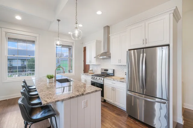 a kitchen with stainless steel appliances granite countertop a refrigerator a sink dishwasher a stove and white countertops with wooden floor