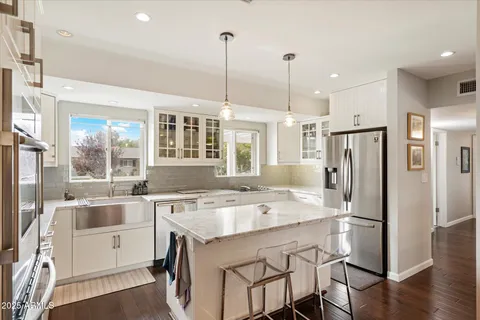 a kitchen with a stove a sink a kitchen island with chairs and white cabinets