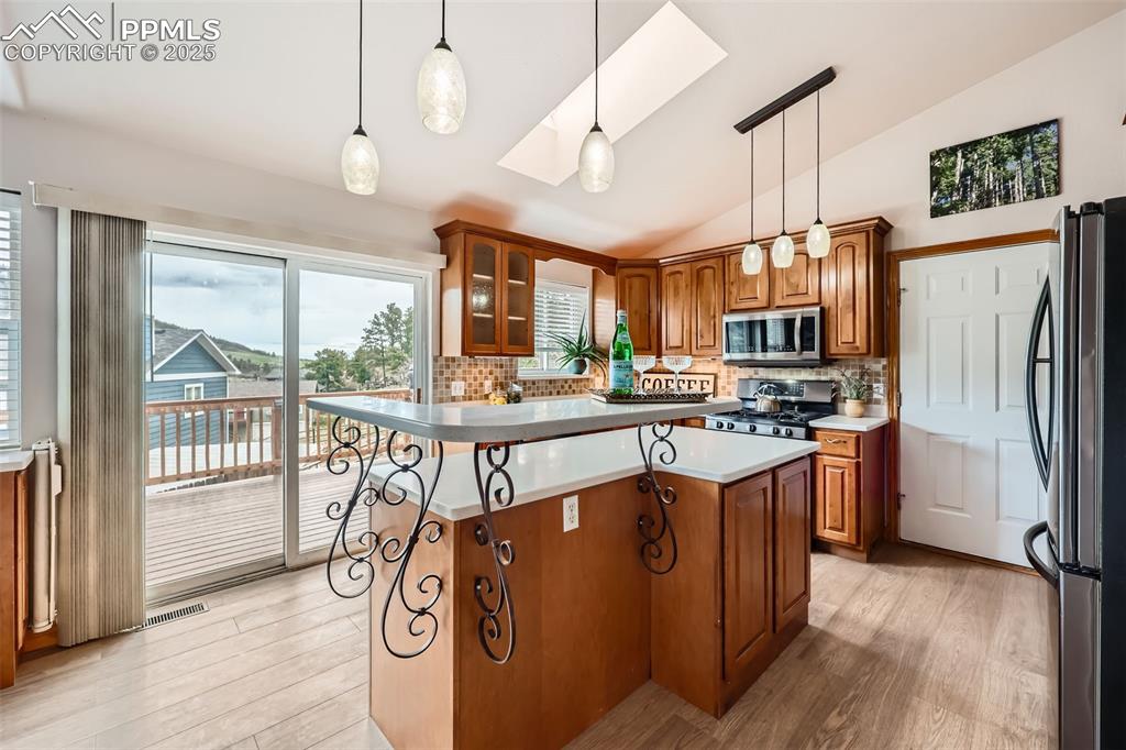 151 Star View Circle Palmer Lake, CO 80133 - Photo 11 of 36 Kitchen featuring appliances with stainless steel finishes, brown cabinets, light wood finished floors, and vaulted ceiling