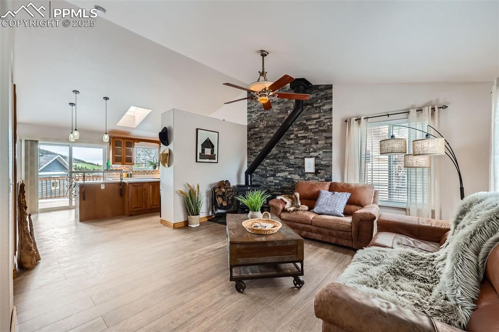 151 Star View Circle Palmer Lake, CO 80133 - Photo 7 of 36 Living room featuring a wood stove, healthy amount of natural light, light wood finished floors, a ceiling fan, and high vaulted ceiling