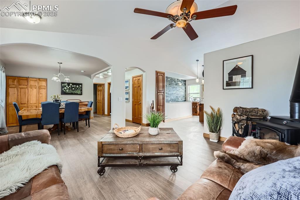 151 Star View Circle Palmer Lake, CO 80133 - Photo 9 of 36 Living room featuring arched walkways, light wood-type flooring, a wood stove, ceiling fan, and vaulted ceiling