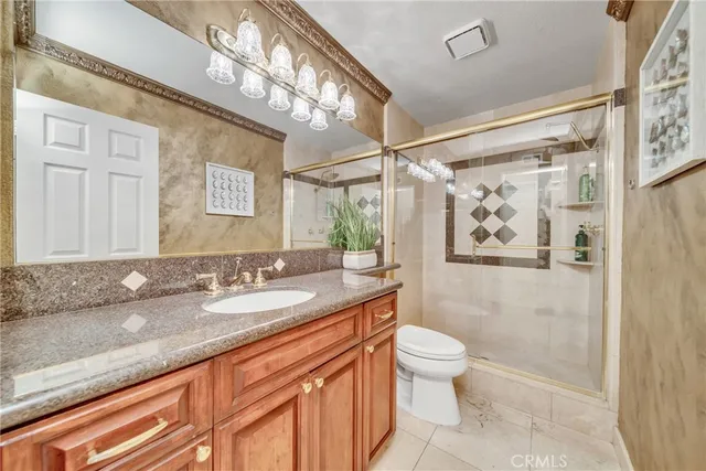 a bathroom with a granite countertop sink a toilet a mirror a vanity and shower