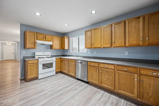 a kitchen with granite countertop wooden floors stainless steel appliances a sink and cabinets