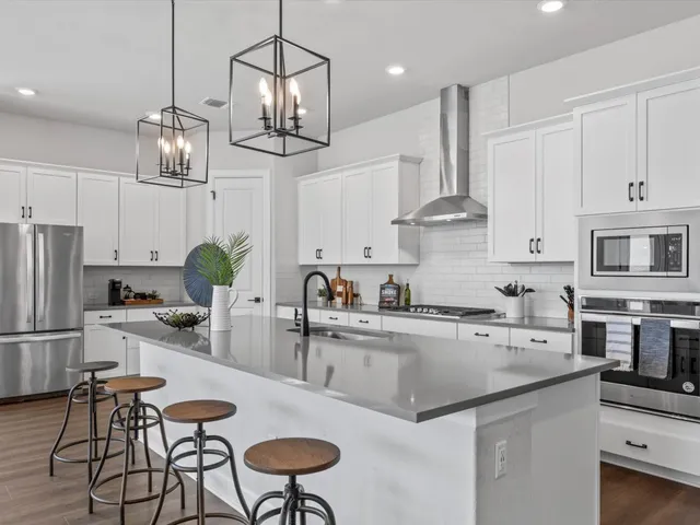 a kitchen with stainless steel appliances a stove a sink a refrigerator and chairs