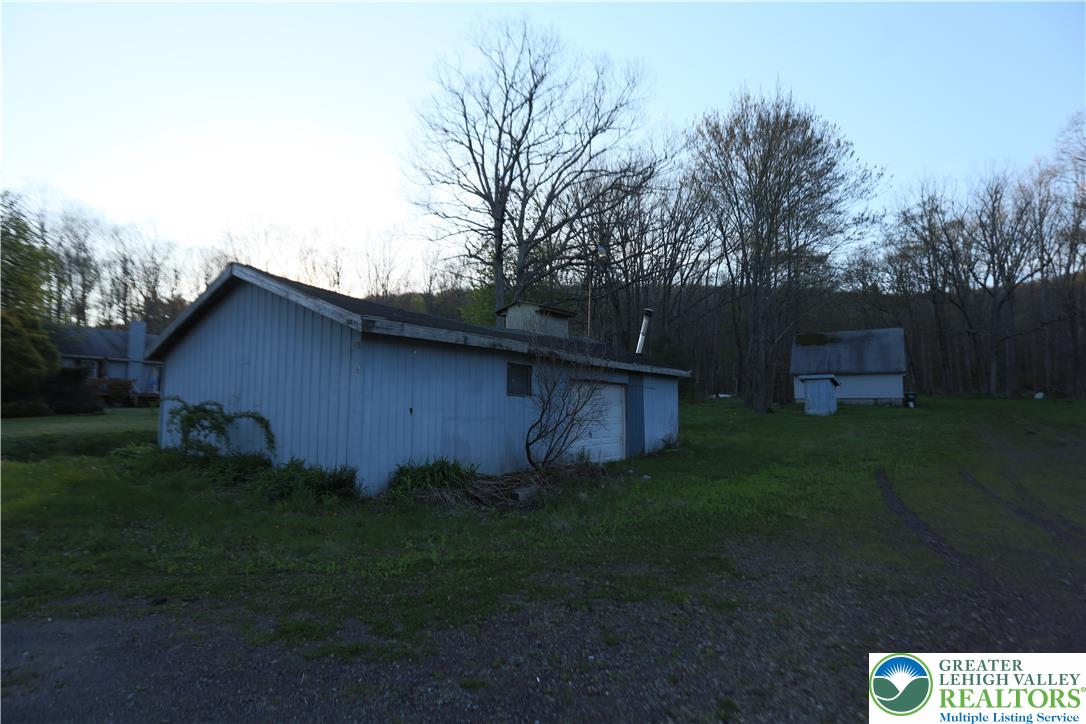 5444 Quakake Road Weatherly, PA 18255 - Photo 12 of 21 A rural outbuilding with pale blue siding sits on a grassy hill, backed by a dense line of trees.