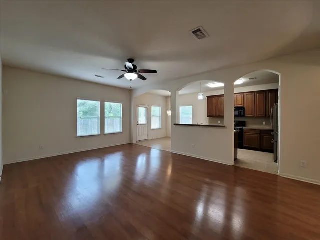 a view of an empty room with wooden floor and a kitchen