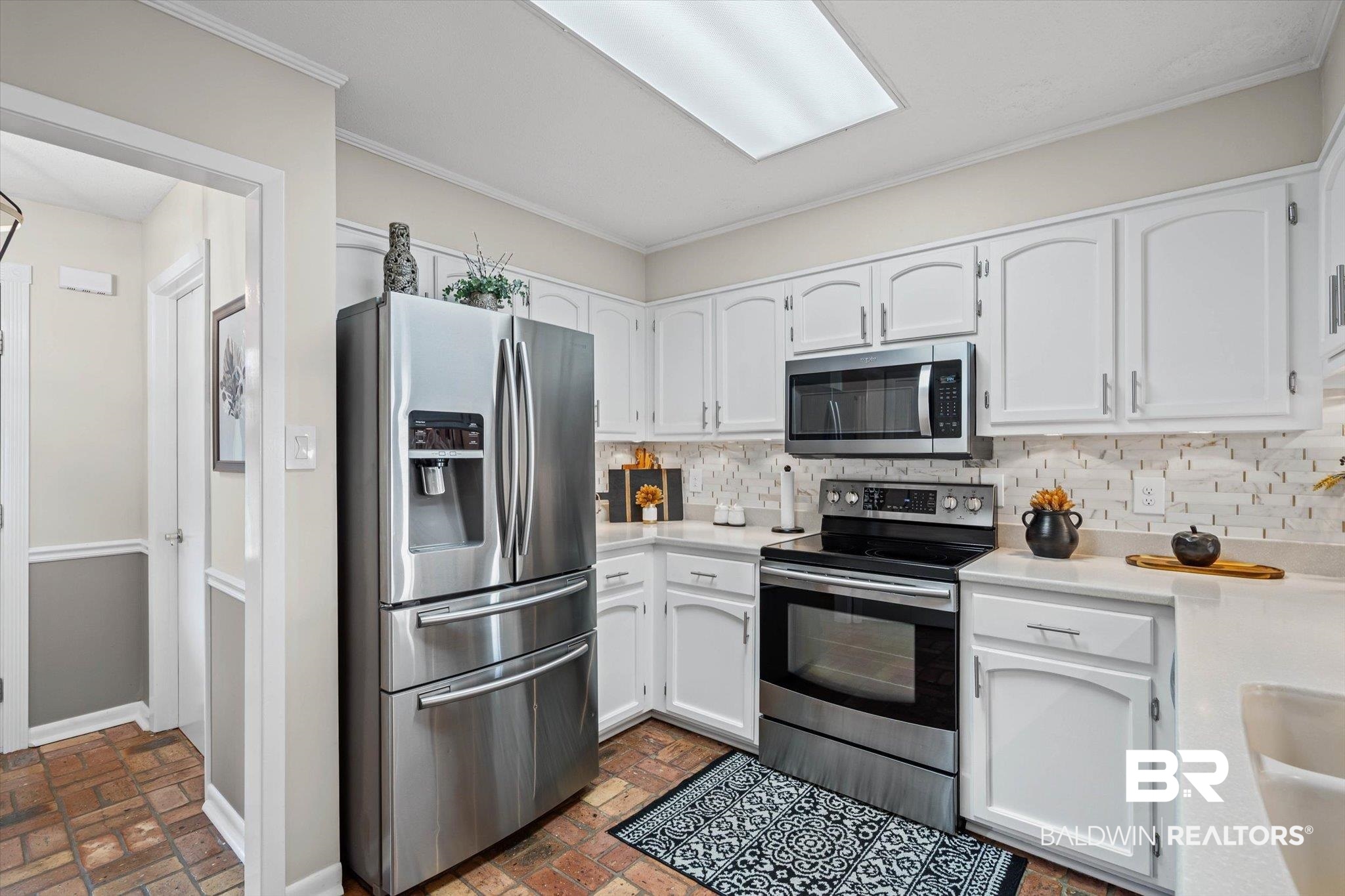 4567 Pine Avenue Saraland, AL 36571 - Photo 10 of 48 Kitchen with appliances with stainless steel finishes, white cabinets, backsplash, ornamental molding, and brick flooring