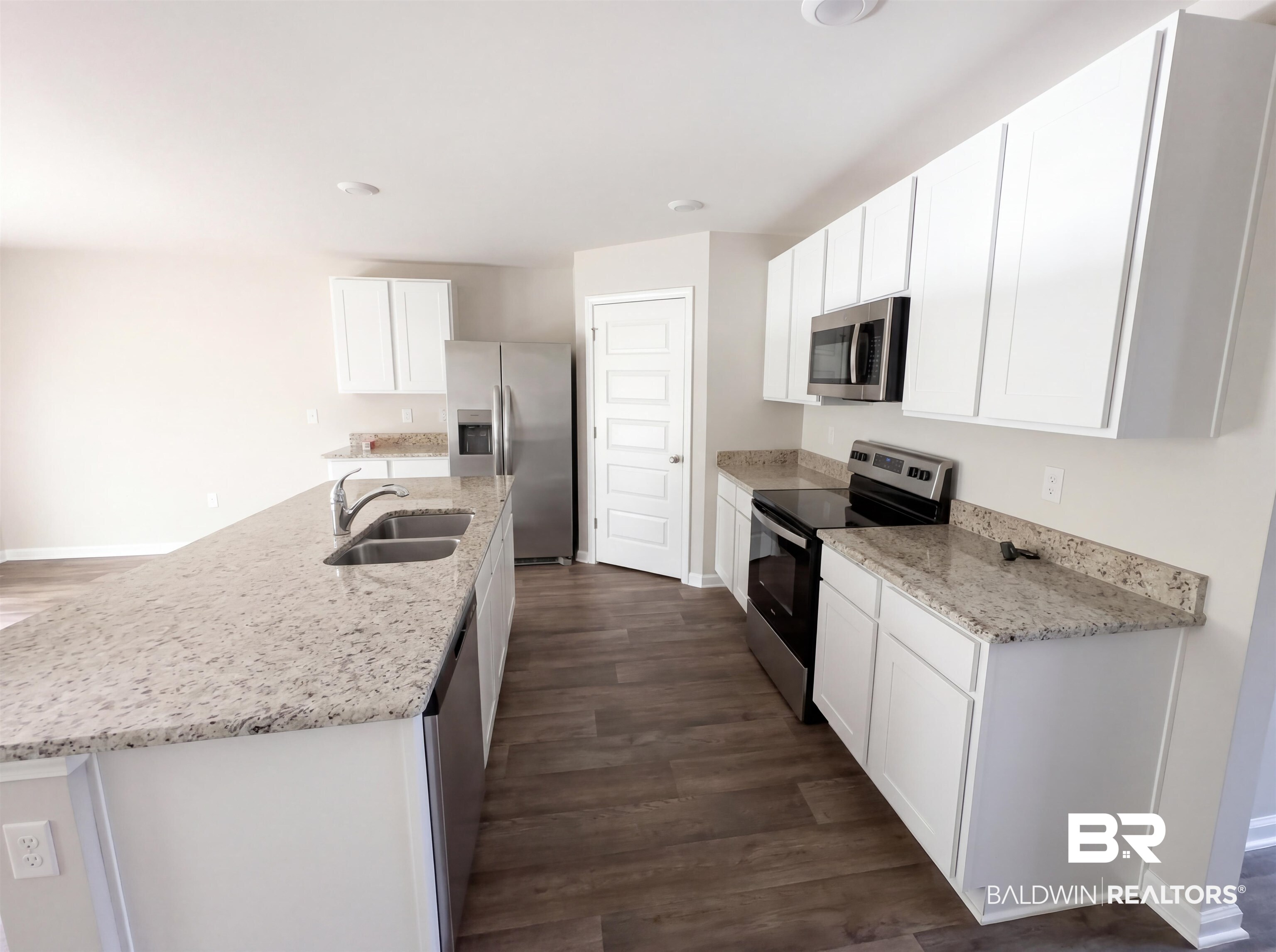 7453 Brompton Drive Foley, AL 36535 - Photo 2 of 15 Kitchen featuring an expansive island with a double basin sink, white cabinetry, granite countertops, wood-finish flooring, and stainless steel appliances