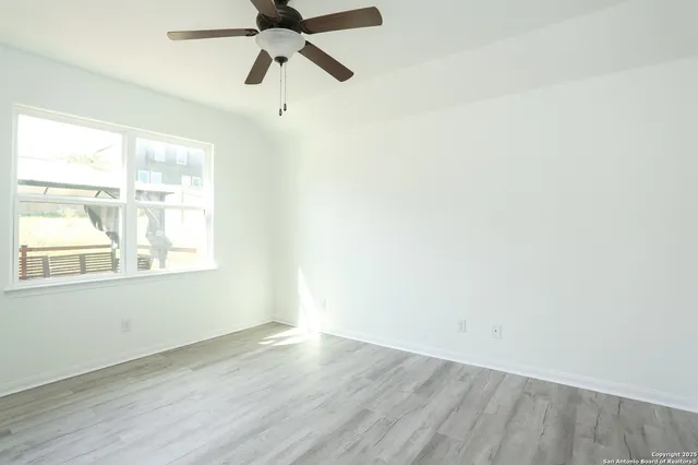 an empty room with wooden floor fan and windows