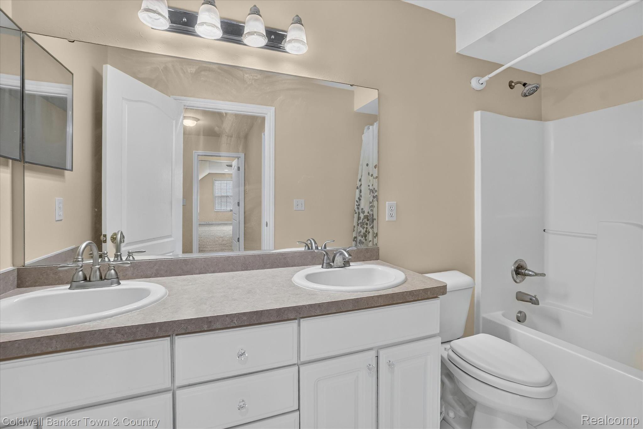 1725 Town Commons Drive Howell, MI 48855 - Photo 37 of 53 Bathroom featuring a double vanity with integrated sinks, a substantial wall-mounted mirror, white cabinetry with crystal knobs, and a white bathtub with an overhead shower