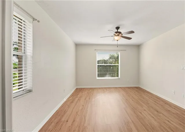 an empty room with wooden floor chandelier fan and windows