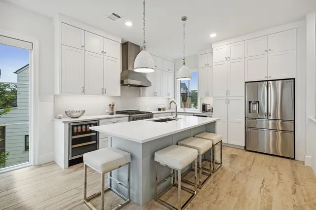 a kitchen with stainless steel appliances a stove a sink a refrigerator and white cabinets with wooden floor