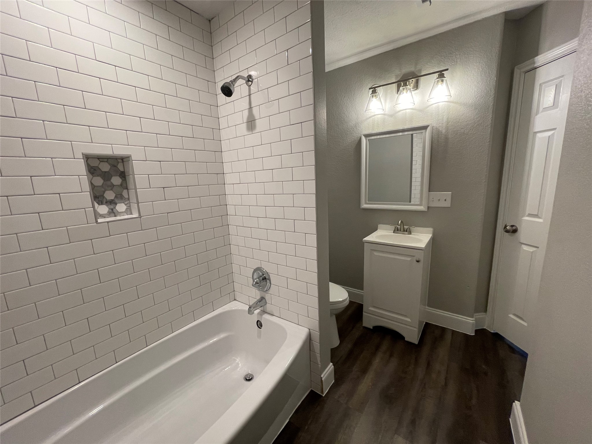 2004 Maple Street Georgetown, TX 78626 - Photo 20 of 31 Bathroom featuring a subway-tiled tub and shower combination with a recessed niche, a white vanity with an integrated sink, a rectangular framed mirror, and wood-finish flooring