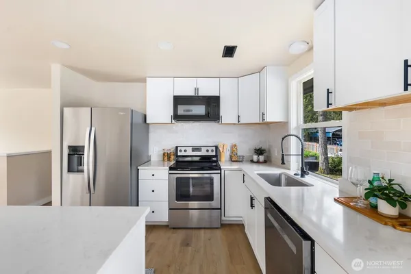 a kitchen with stainless steel appliances a stove a sink a microwave a refrigerator a refrigerator white cabinets and wooden floor