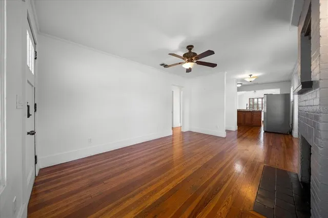 a view of an empty room with wooden floor and a ceiling fan