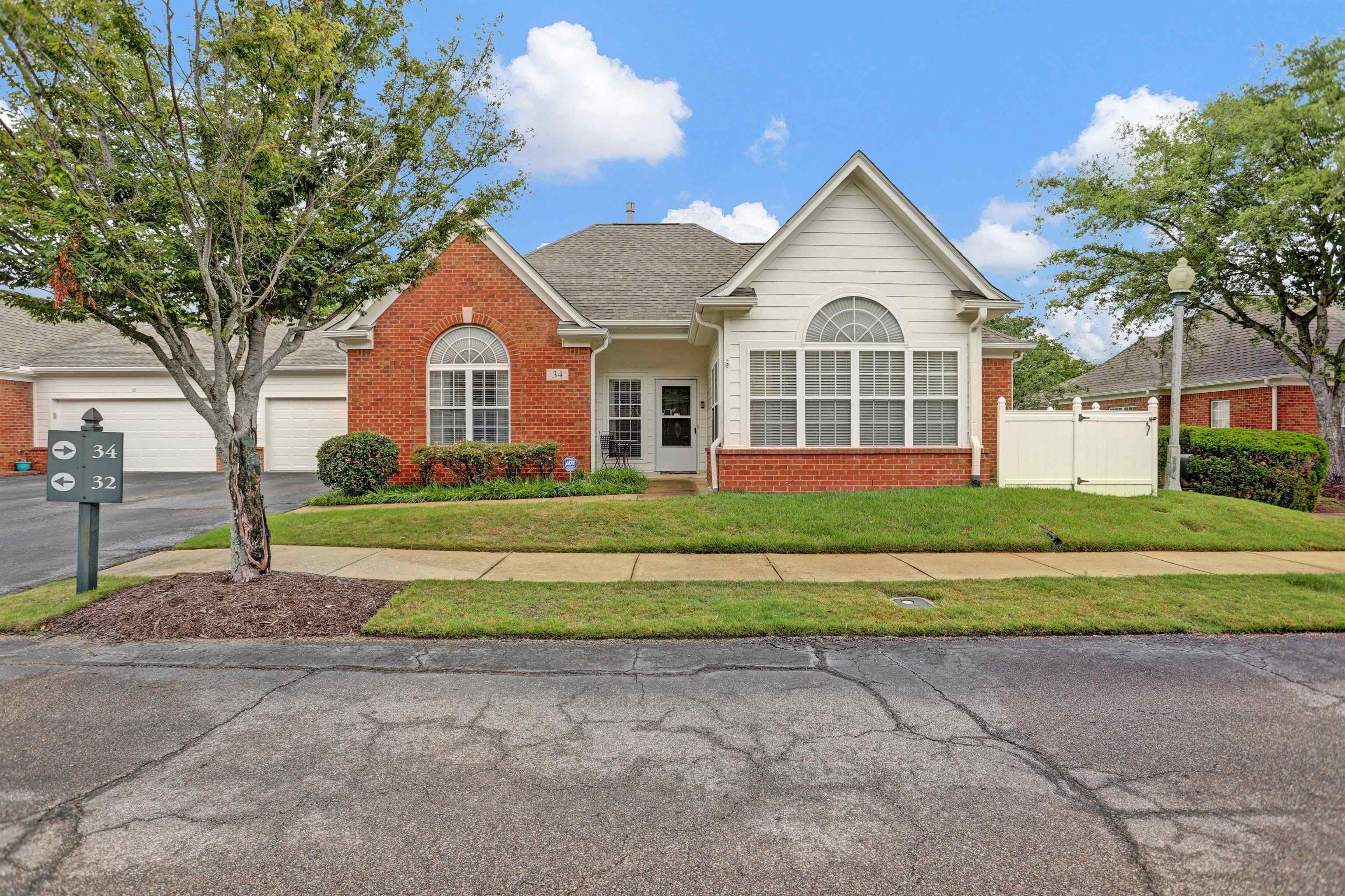 34 Peyton Ridge Drive, Unit 21 Collierville, TN 38017 - Photo 1 of 37 Brick and white siding exterior featuring a prominent arched window, pitched roofline, mature landscaping, and a white privacy fence