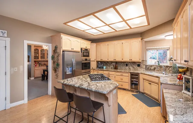 a kitchen with stainless steel appliances granite countertop a stove a refrigerator a oven a sink a dining table and chairs with wooden floor