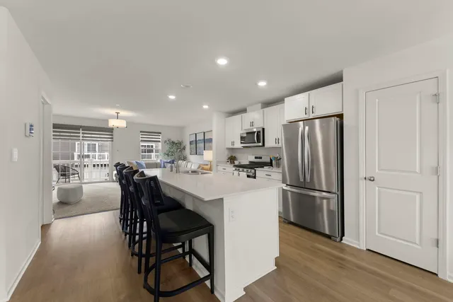 a kitchen with stainless steel appliances a refrigerator a stove a dining table and chairs with wooden floor