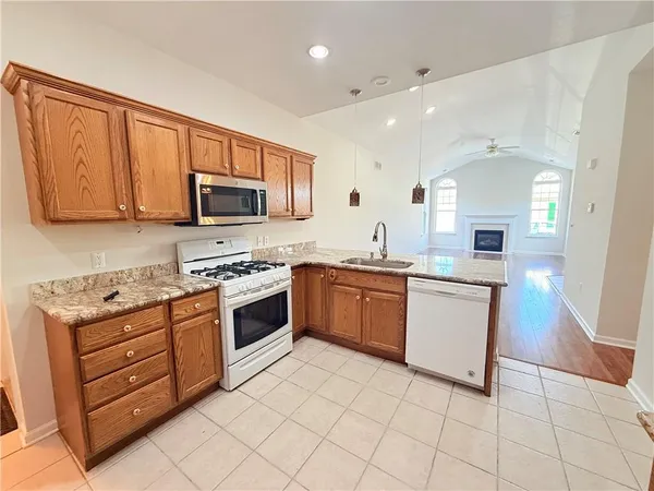 a large kitchen with stainless steel appliances granite countertop a stove top oven a sink dishwasher and a refrigerator with wooden cabinets