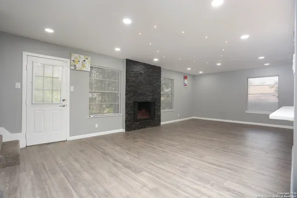 an empty room with wooden floor fireplace and windows