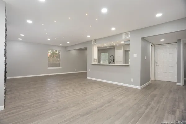 a view of an empty room with wooden floor and a kitchen