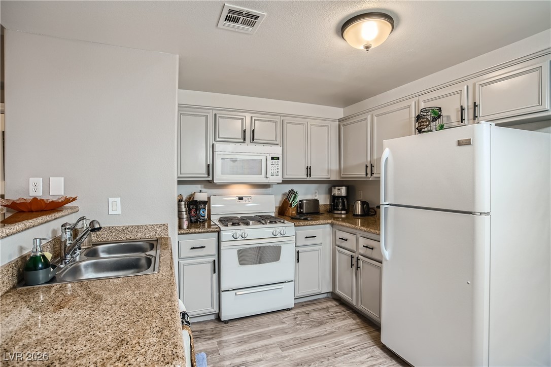 7701 West Robindale Road, Unit 149 Las Vegas, NV 89113 - Photo 6 of 22 Kitchen featuring white appliances, light wood-type flooring, and light stone counters