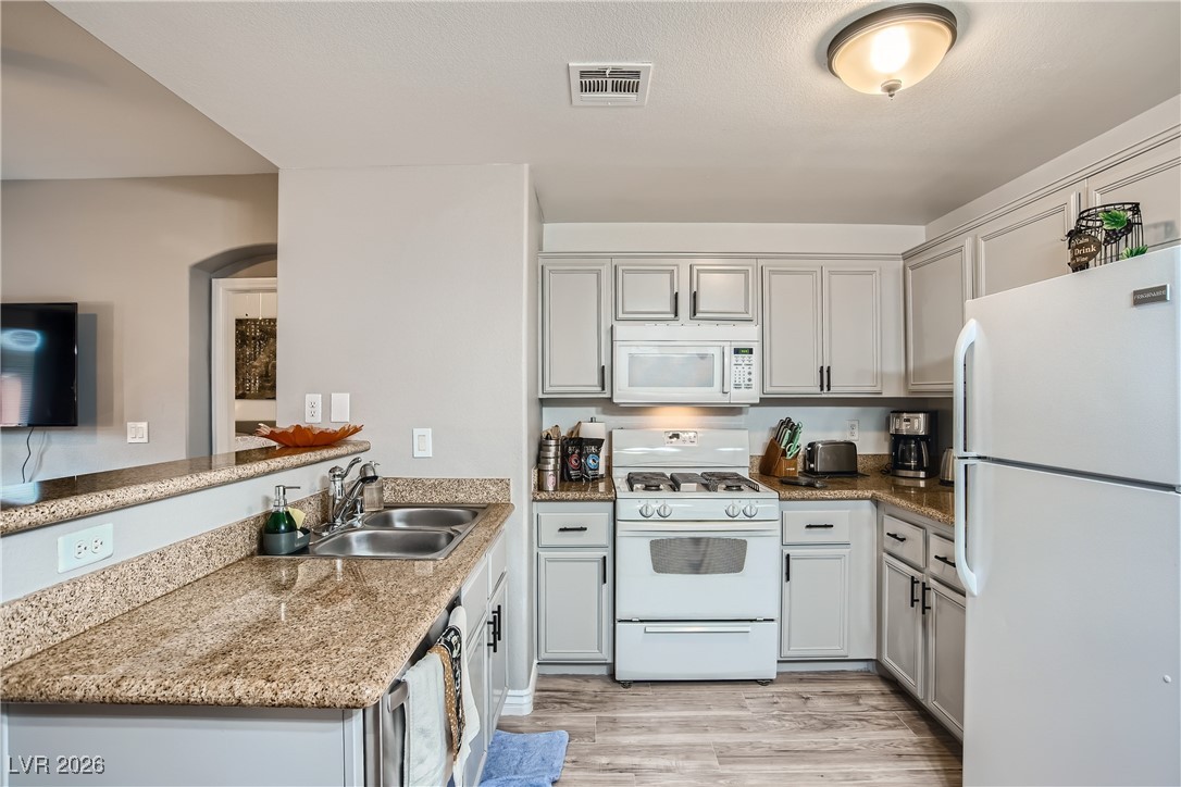 7701 West Robindale Road, Unit 149 Las Vegas, NV 89113 - Photo 8 of 22 Kitchen with white appliances, light wood finished floors, a peninsula, light stone countertops, and gray cabinets