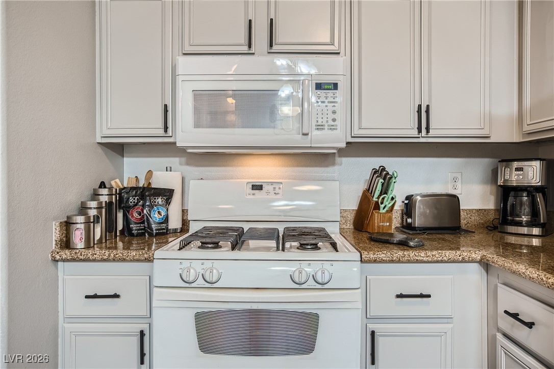 7701 West Robindale Road, Unit 149 Las Vegas, NV 89113 - Photo 9 of 22 Kitchen featuring white appliances, white cabinetry, and dark stone counters