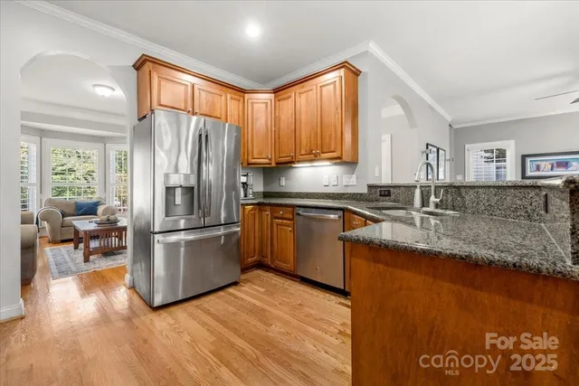 a kitchen with stainless steel appliances granite countertop a refrigerator a sink dishwasher a stove with wooden cabinets and wooden floor