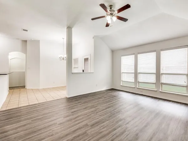 an empty room with wooden floor and windows with ceiling fan